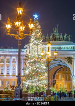 Saint-Petersburg, Russia - Jan 18 2021, vertical view of ornate Christmas tree on palace square, with a glowing street lamp in foreground and Arch of Stock Photo