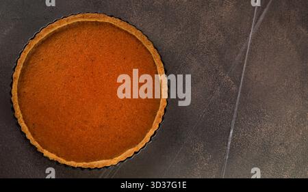 A freshly baked pumpkin pie sits on a dark countertop, cooling down. The rich filling glistens, inviting festive celebrations and warm gatherings with Stock Photo