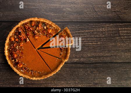 A freshly baked pie sits on a rustic wooden table, showcasing a rich filling topped with nuts. Slices have been cut for sharing at a warm family gathe Stock Photo