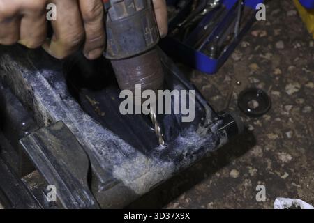 Close up of skilled mechanic hand drilling hole in black plastic component for repair. focused worker using power tool for maintenance work inside gar Stock Photo