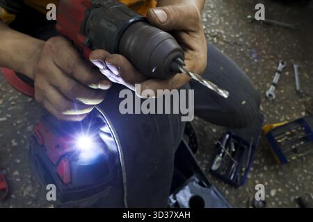 Concentrated worker hand holding power tool drill for repair. mechanic in workshop performing manual labor with cordless electric drill, showing focus Stock Photo