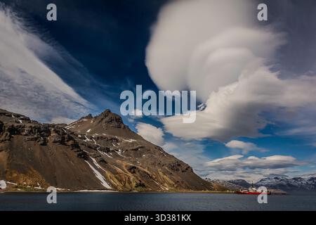 coastal region on South Georgia Island, with steep mountainside and unusual white cloud in the blue sky. Like a smoking volcano. Stock Photo