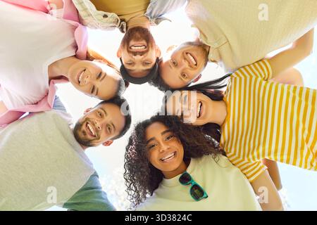 Friends together, group of young adults standing closely together in circle, looking downwards Stock Photo