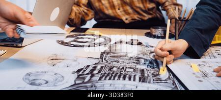 A group of professionals engages in a focused session, reviewing detailed engineering drawings and collaborating on a mechanical project at a design Stock Photo