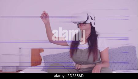 Woman wearing olive jumpsuit and headset experiencing virtual reality on bed, with white device Stock Photo