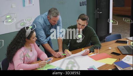 Collaborating coworkers sketching on paper on conference table, with sticky notes and digital icons Stock Photo
