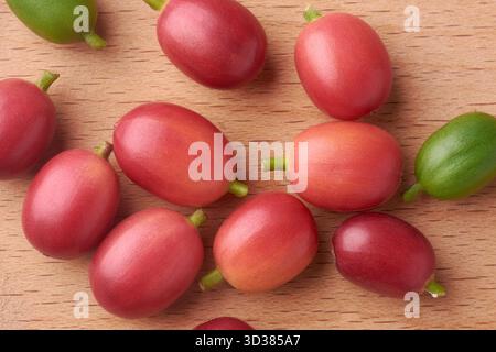macro close-up of coffee cherries scattered on light brown wooden surface, ripe red and green unripe berries with stems taken from above Stock Photo