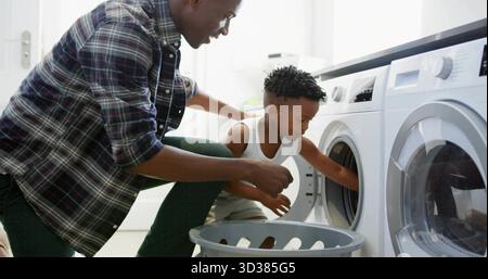 Helping parent and child loading laundry into front-loading washer in laundry room with gray basket Stock Photo