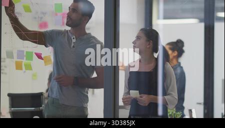 Brainstorming colleagues writing on glass partition at office, with sticky notes and marker Stock Photo