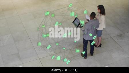Colleagues examining holographic financial data overlay in corporate lobby, with laptop and tablet Stock Photo