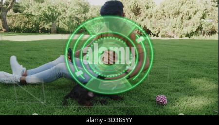 Sitting Asian man holding smartphone on park lawn, with brown backpack and rope toy Stock Photo