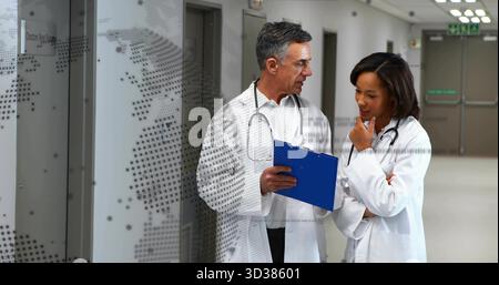 Consulting two doctors in lab coats holding blue clipboard in corridor by dotted glass panel Stock Photo
