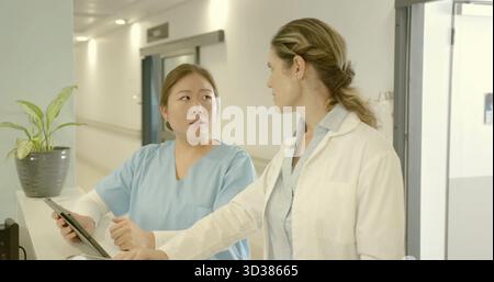Discussing patient info medical professionals in scrubs and lab coats using tablet at nurse station Stock Photo