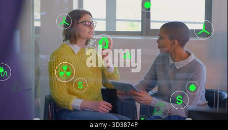 Gesturing businesswomen discussing sustainable finance holding tablet in office with floating icons Stock Photo