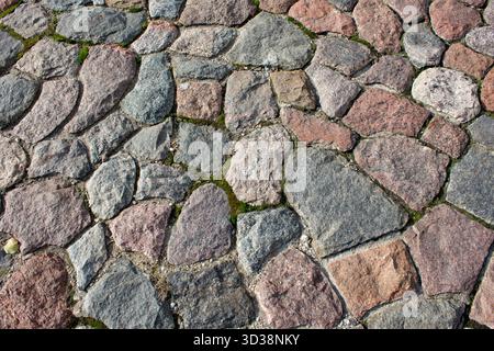 Fragment of a road made of granite stones. Paving stones on the sidewalk. Paving stones made of granite stones on an old road. Stone background. Stock Photo