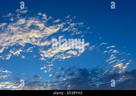 Warm sunrise light paints the clouds in soft golden and blue tones, creating a calm and inspiring morning sky atmosphere. Stock Photo
