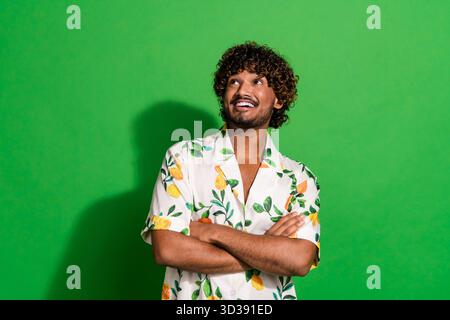Photo of confident dreamy latin guy dressed print shirt arms crossed looking empty space isolated green color background Stock Photo