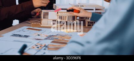 A dynamic scene of a teamwork brainstorming session involving hands working on an architectural model and design sketches, emphasizing collaboration Stock Photo