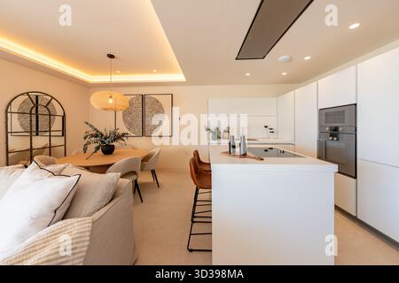 Open plan kitchen and dining room with modern white cabinets and island in holiday home Stock Photo