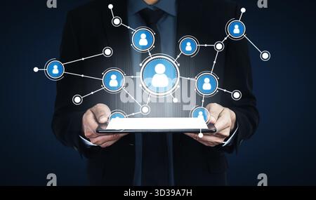 A businessman holds a tablet displaying user icons connected by lines, symbolizing the concept of digital networking and communication in the modern Stock Photo