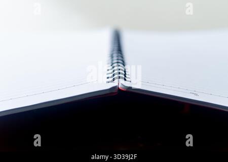 A close-up angled shot of an open spiral-bound notebook. The clean, white, lined pages are empty. Perfect background for study or notes. Stock Photo