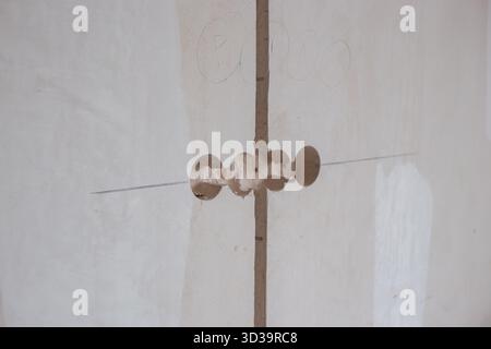 A white, unfinished wall with marked lines and four round holes for outlets or switches, representing renovation and construction stages. Stock Photo
