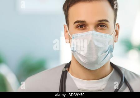 Close up shot of young male doctor wearing protective face mask, medical uniform, focused at camera Stock Photo