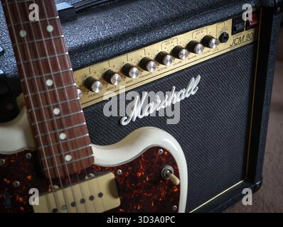 Close up detail image of Marshall JCM900 Series Guitar Amplifier and Logo, with a Fender Jazzmaster electric guitar resting against it Stock Photo