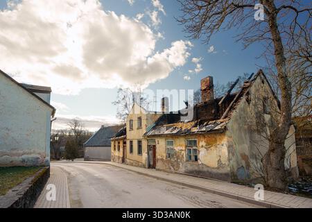 A striking horizontal view of an old, abandoned, and severely damaged building with a collapsed, burned roof and peeling yellow plaster on a street in Stock Photo