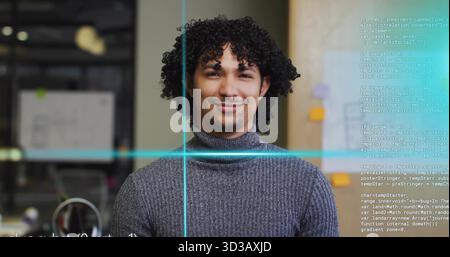 Smiling developer wearing grey sweater at office cubicle, with computer monitor and code overlay Stock Photo