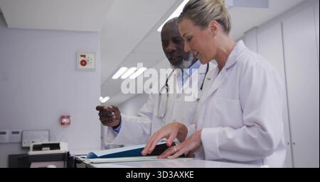 Reviewing doctors collaborating at nurses station corridor with patient file folder and keyboard Stock Photo
