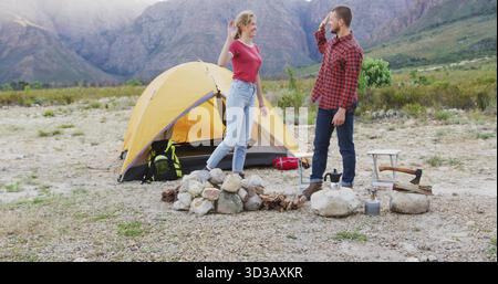 Raising hands man and woman greeting each other at rocky campsite, with yellow tent, camping gear Stock Photo