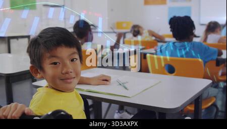 Smiling boy in yellow t-shirt writing in notebook at white desk in school classroom, with pencil Stock Photo