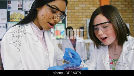 Mixing teen students wearing lab coats adding red solution from beaker using dropper in science lab Stock Photo