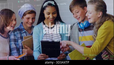 Gathering five students leaning over tablet in bright classroom, with notebooks books headphones Stock Photo