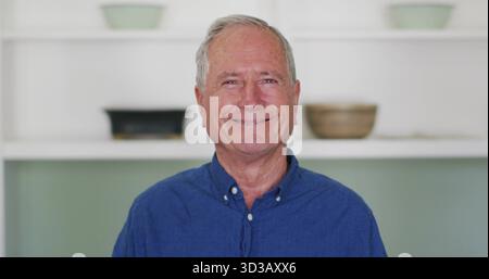 Standing senior wearing blue shirt at home, with white shelves, planters, black dish  and  beige bow Stock Photo