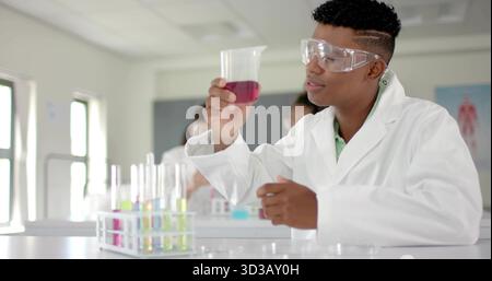 Holding purple solution beaker, teen wearing lab coat in classroom, with test tube rack, copy space Stock Photo