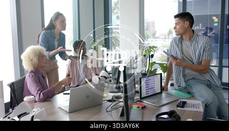 Collaborating colleagues discussing tech presentation at office table, with laptops and VR headset Stock Photo