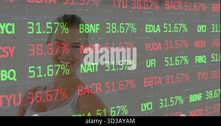 Smiling woman standing behind transparent display at trading floor, displaying tickers in red green Stock Photo
