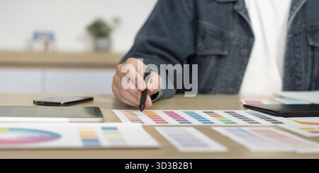 A designer selecting colors from a palette while using a digital pen on a tablet, showcasing creativity in a modern workspace Stock Photo