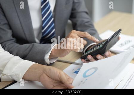 Colleagues collaborating on financial calculations, utilizing a calculator to evaluate fiscal data and reports Stock Photo
