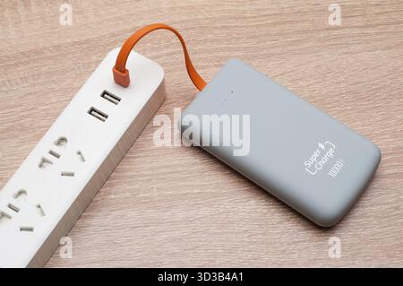 The gray power bank is charged via a wire from a white extension cord with usb outputs. Objects on the table top view. Super Charge is written Stock Photo