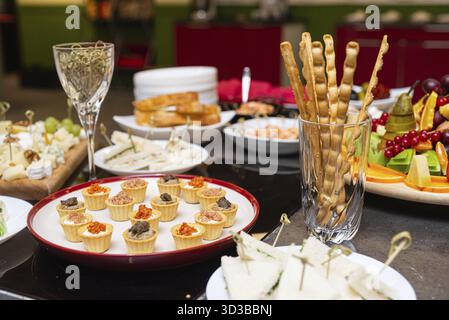 Food, Assorted finger foods and snacks on a buffet table, including mini tarts, breadsticks, sandwiches, cheese, and fresh fruit Stock Photo