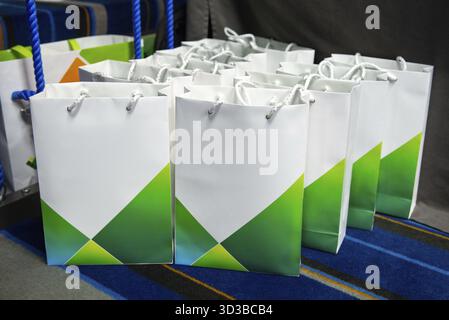 Food, Multiple white and green corporate gift bags with rope handles arranged on a blue carpet, prepared for an event or giveaway Stock Photo