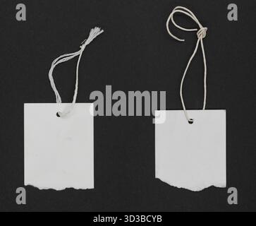 Torn white paper labels or tag with thread tie on black grunge paper background. White labels with copy space Stock Photo