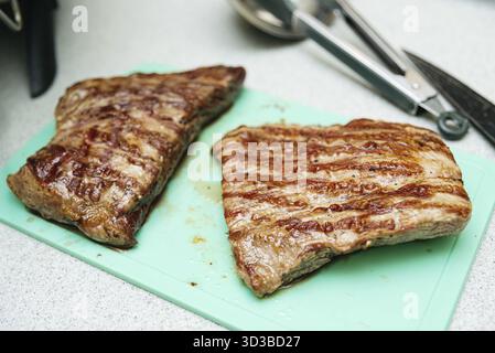 Food, Two juicy grilled flank steaks with char lines placed on a green cutting board, ready for slicing and serving Stock Photo