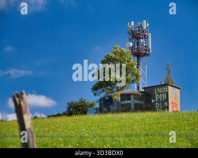 Espelette, France - Oct 10 2025: In Espelette, France, a hilltop cell tower overlooks a meadow and a small building painted with a Basque independence message against a clear blue sky. Stock Photo