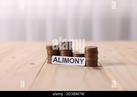 Paper note with word Alimony and stacked coins on wooden table, closeup Stock Photo