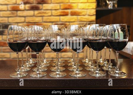 Food, A row of elegant wine glasses filled with red wine, neatly arranged on a bar counter against a warm brick wall background Stock Photo
