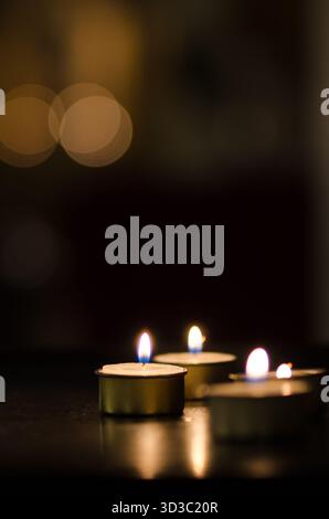 Warm and serene close-up of lit tealight candles in a dim setting. The soft bokeh lights in the background add to the peaceful ambiance, perfect for m Stock Photo